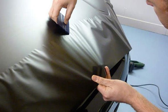 Hands using a squeegee to apply film to a glossy car hood surface