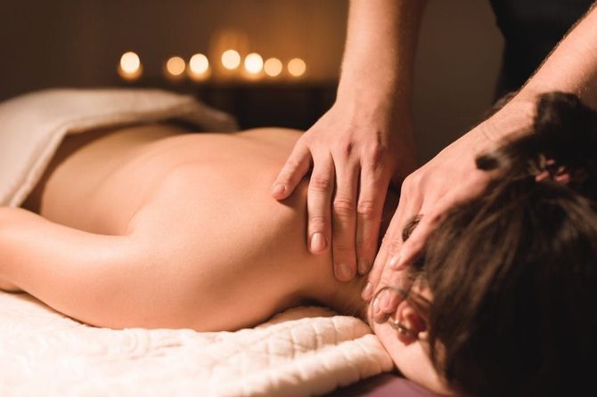 Spa massage with hands on a woman's back, surrounded by orchids and candles
