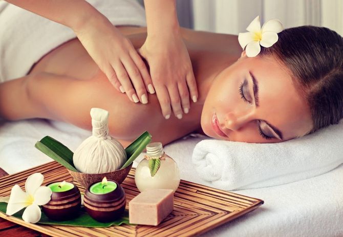 Woman receiving a spa massage with candles, flowers, and massage stones on a tray