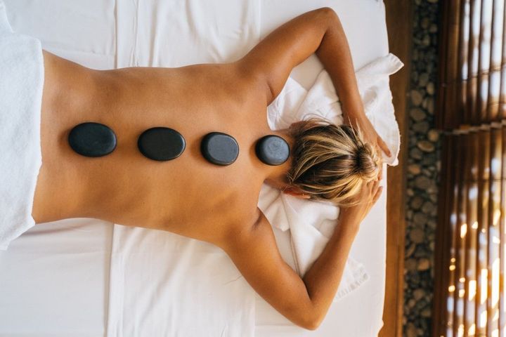 Person lying face down on a massage table with four hot stones on their back