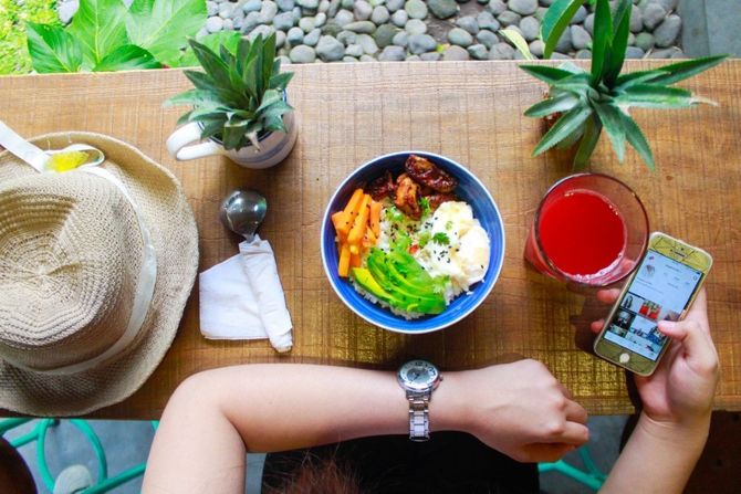 Overhead view of a table with food, hat, drink, plants, and a person using a smartphone