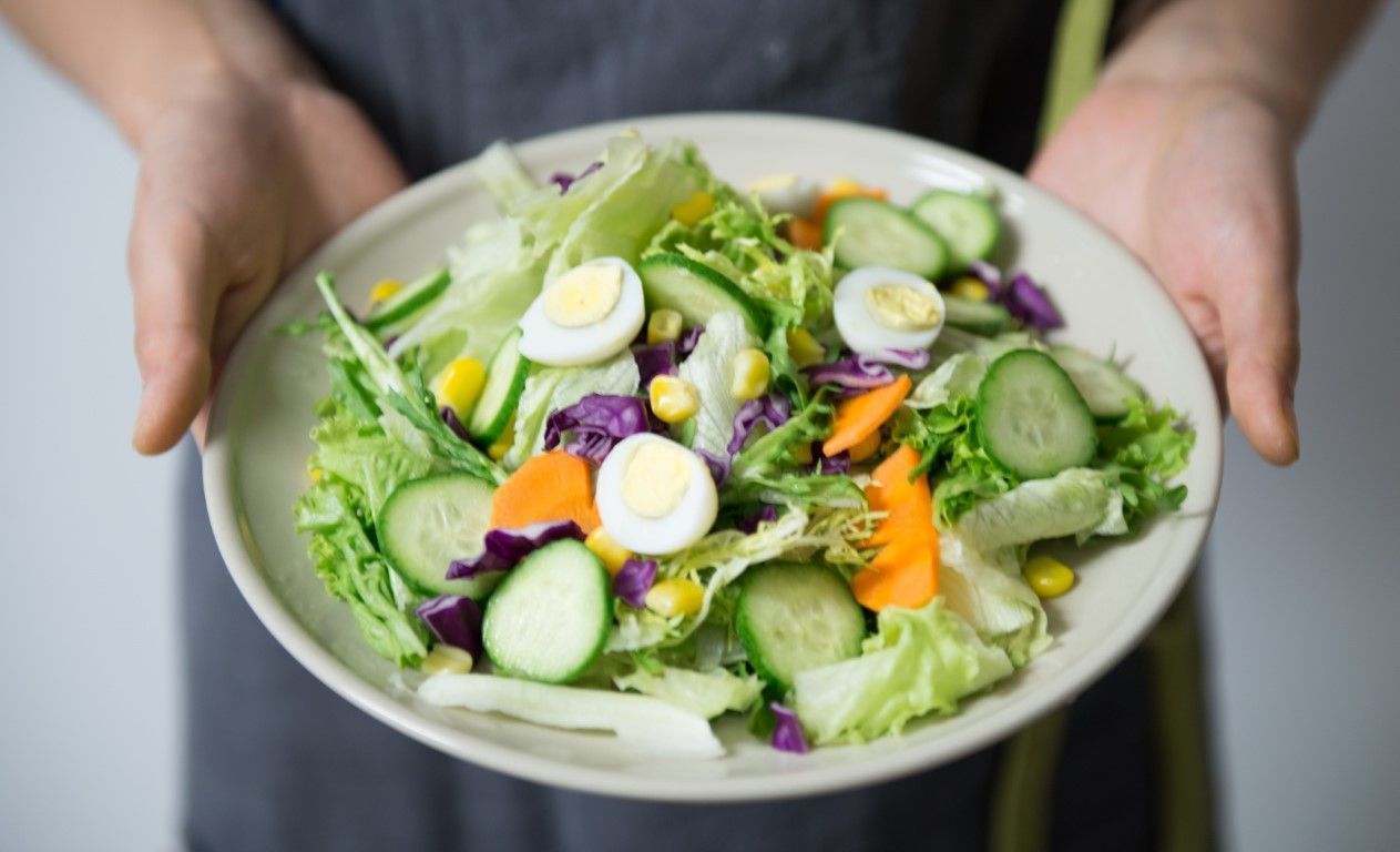 Hands holding a bowl of fresh salad with cucumber, avocado, purple cabbage, and boiled egg slices