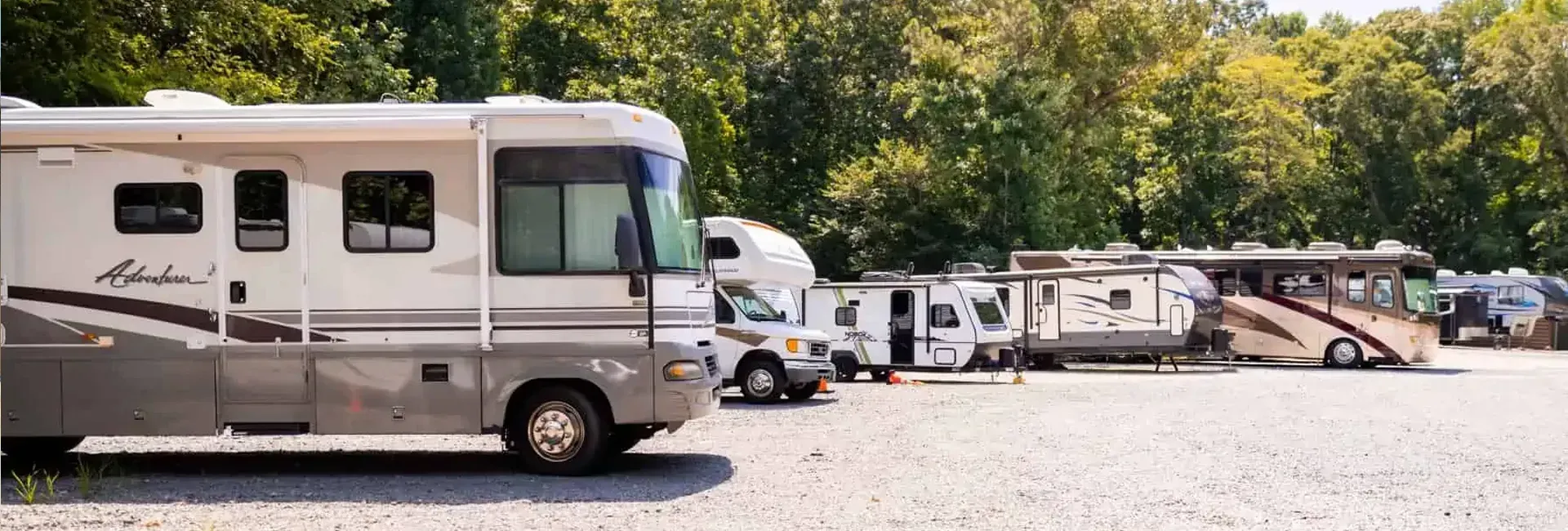 Several RVs parked on gravel, backed by trees.