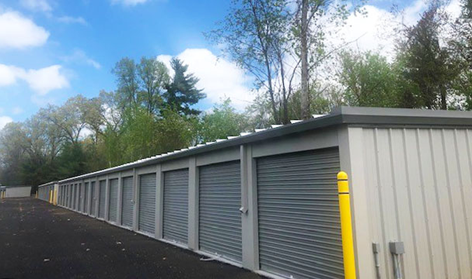 Storage units in a row with gray doors, surrounded by trees and blue sky.