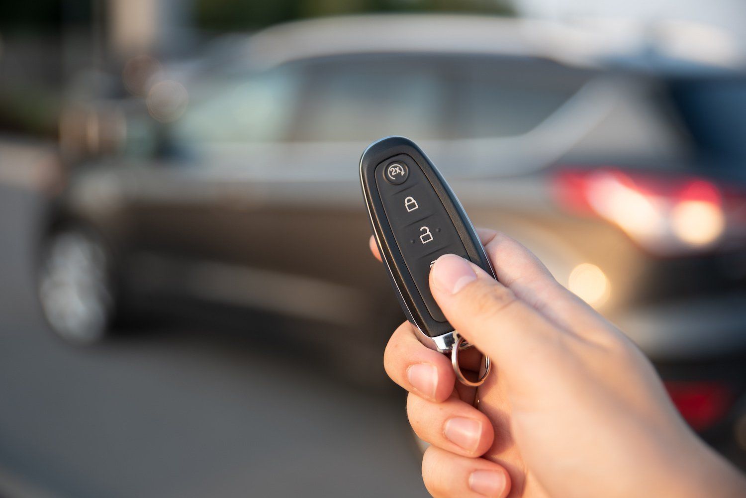 A person is holding a remote control in front of a car.