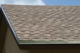 Close-up of a house roof with gray shingles and a blue sky background