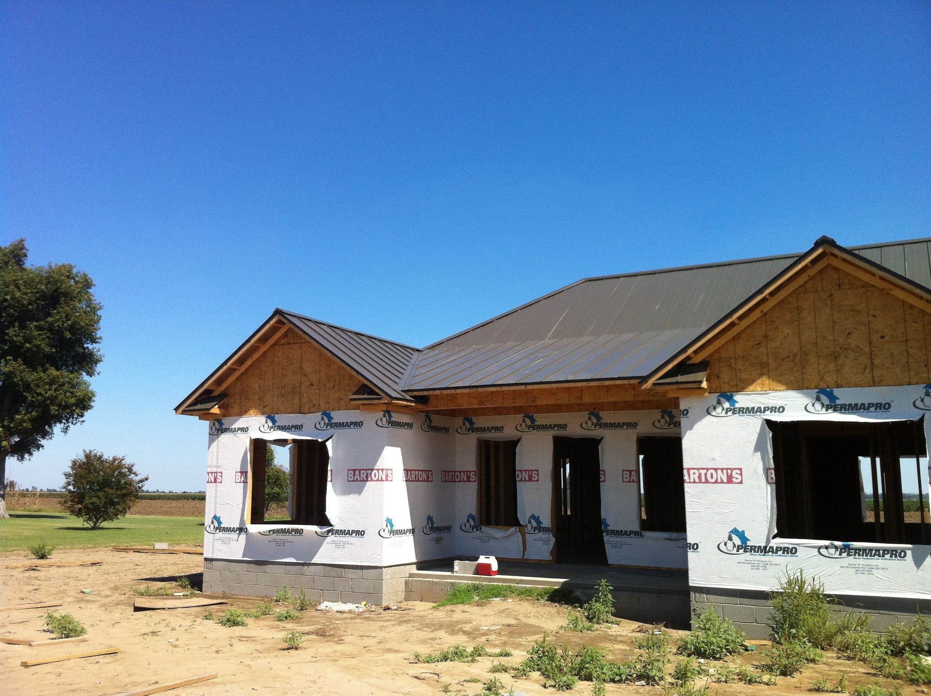 Partially built white house with brown roof in a rural field under a clear blue sky