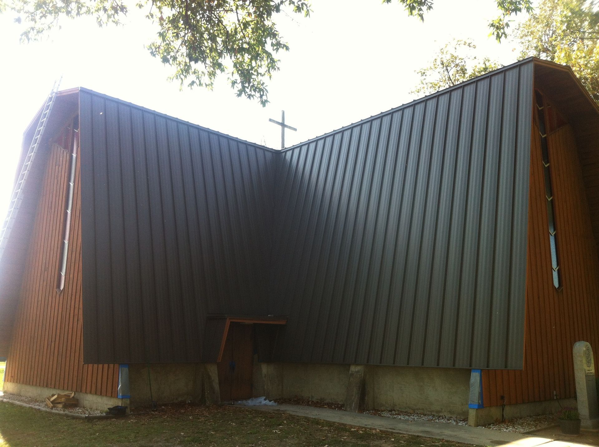 Modern church with steep dark roof and wooden sides, viewed from below against a bright sky