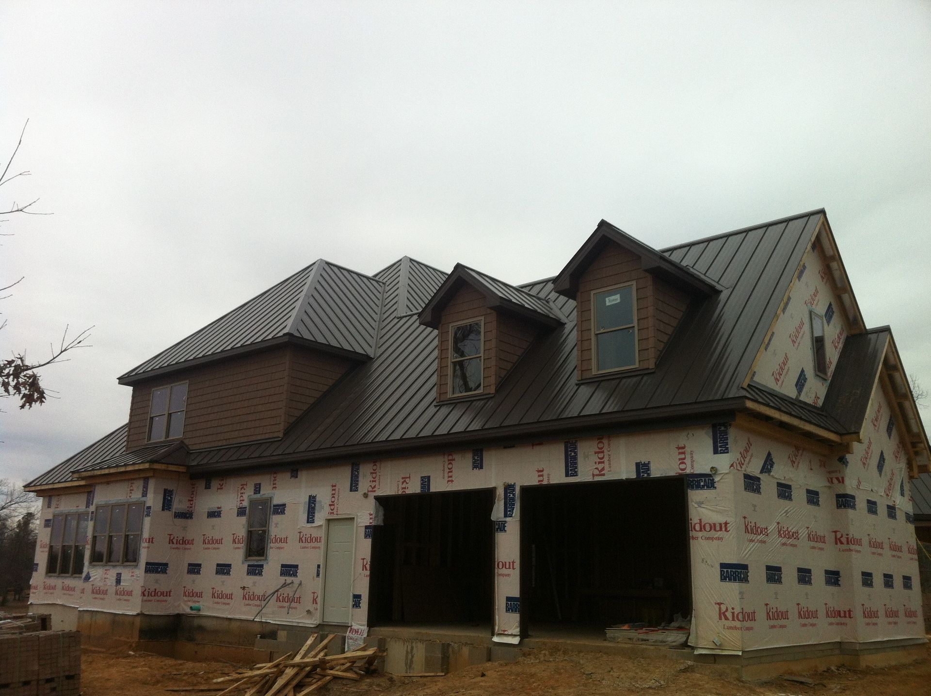 House under construction with dark metal roof and unfinished exterior wrapping.
