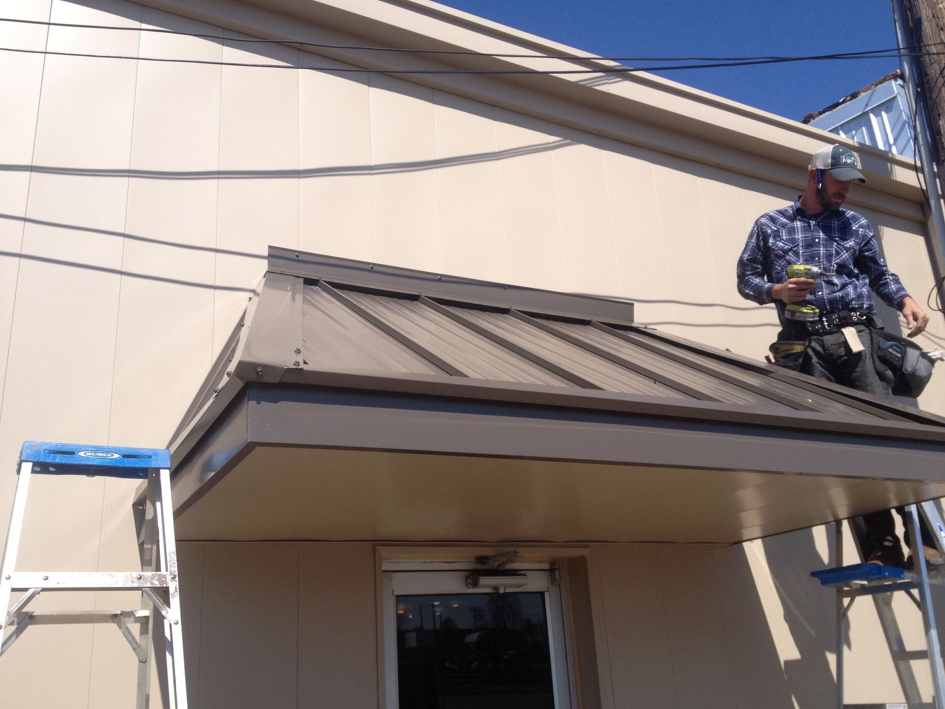 Worker on a ladder repairing the metal awning above a building entrance