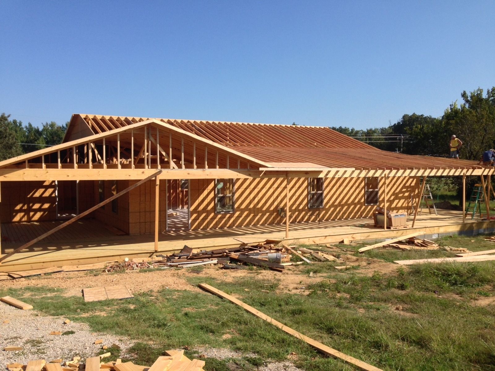 Partially built wooden house with exposed roof framing and red tiles on a grassy lot