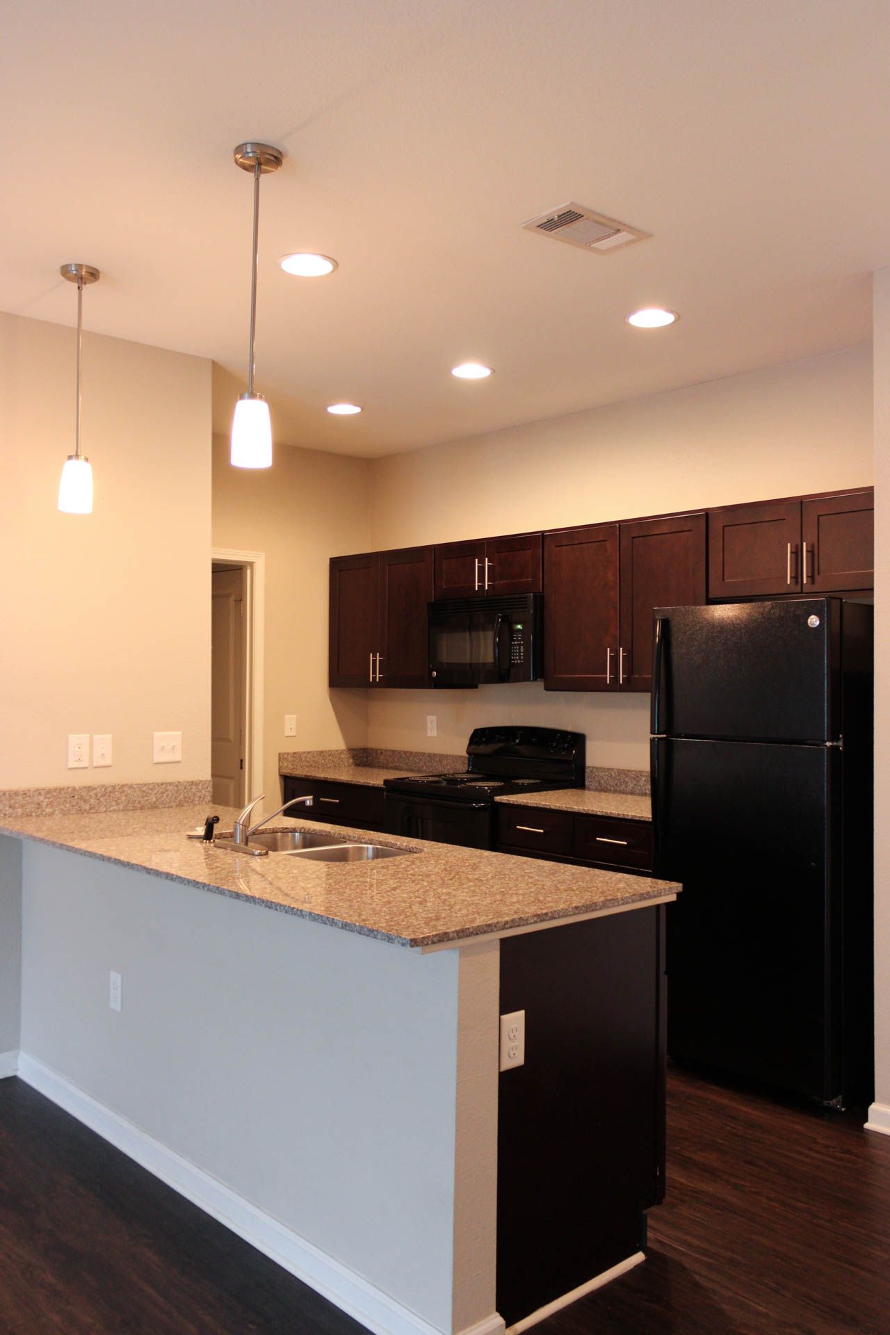 A kitchen with granite counter tops , a black refrigerator , a microwave , and a sink.