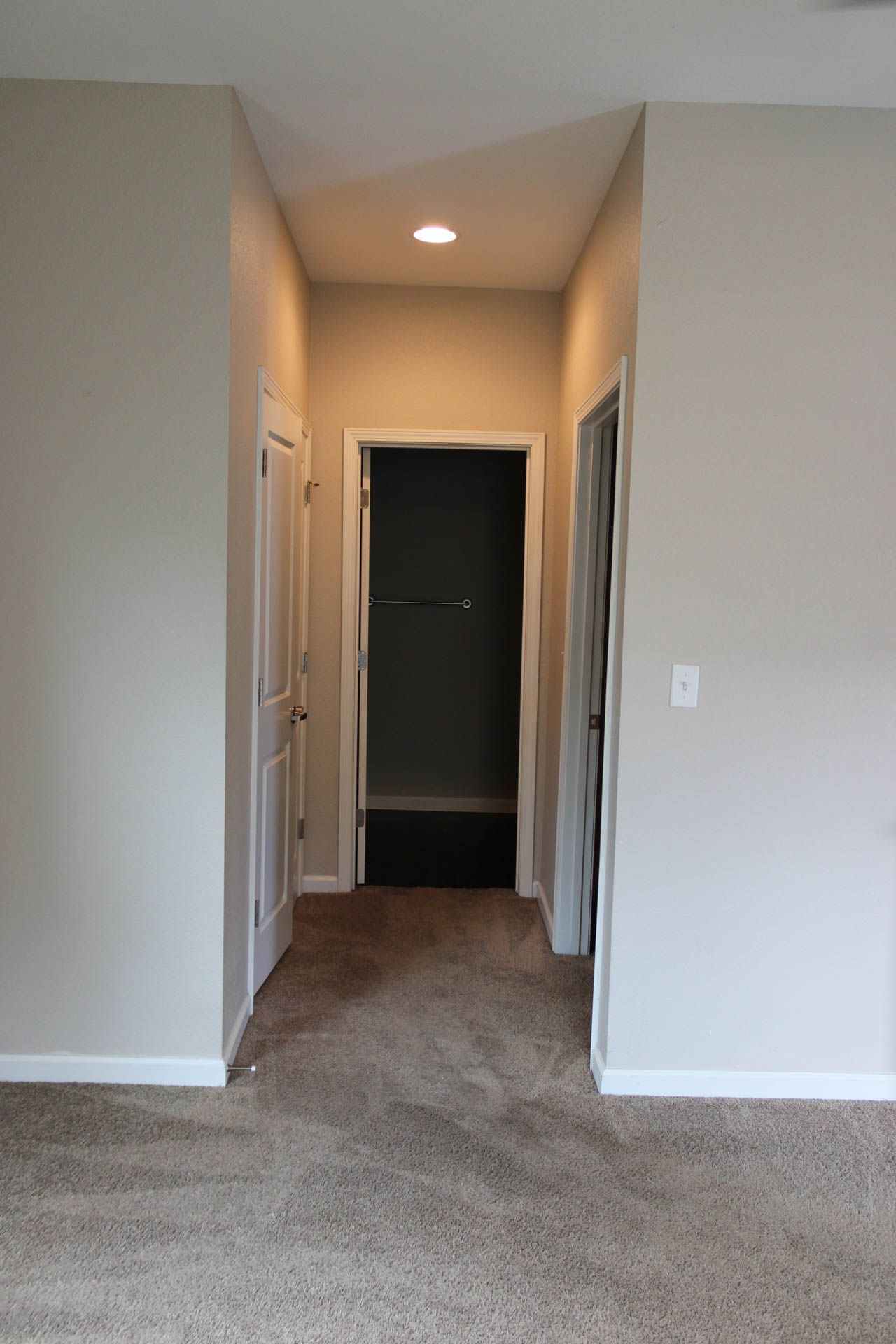 A hallway leading to a bathroom and a walk in closet in a house.