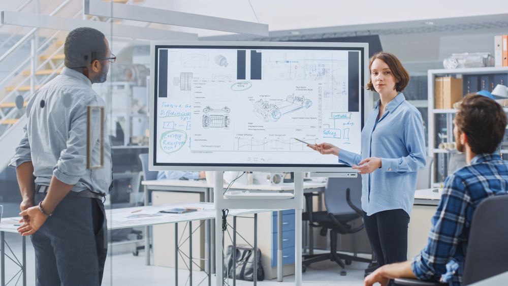 Three People Discuss a Large Engineering Diagram on a TV in a Bright Office — MATV Systems Australia Pty Ltd in Wickham, NSW