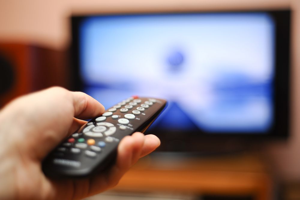 Hand Holding a Remote Control Aimed at a Blurry TV Screen — MATV Systems Australia Pty Ltd in Wickham, NSW