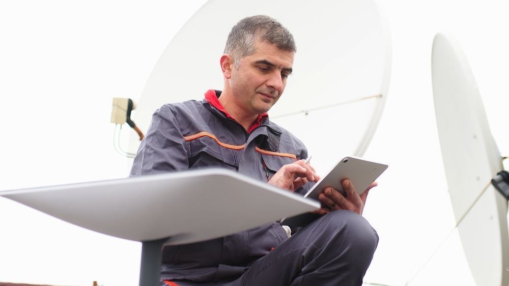 Man on a Rooftop Using a Tablet Beside a Satellite Dish — MATV Systems Australia Pty Ltd in Wickham, NSW