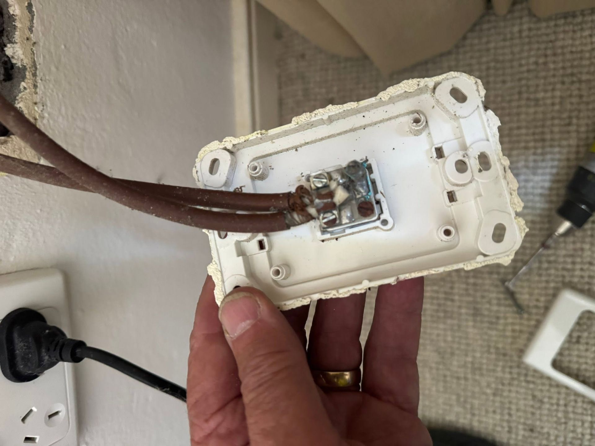 White electrical outlet cover with exposed wiring, lying on a carpeted floor near a wall socket. — MATV Systems Australia Pty Ltd in Wickham, NSW