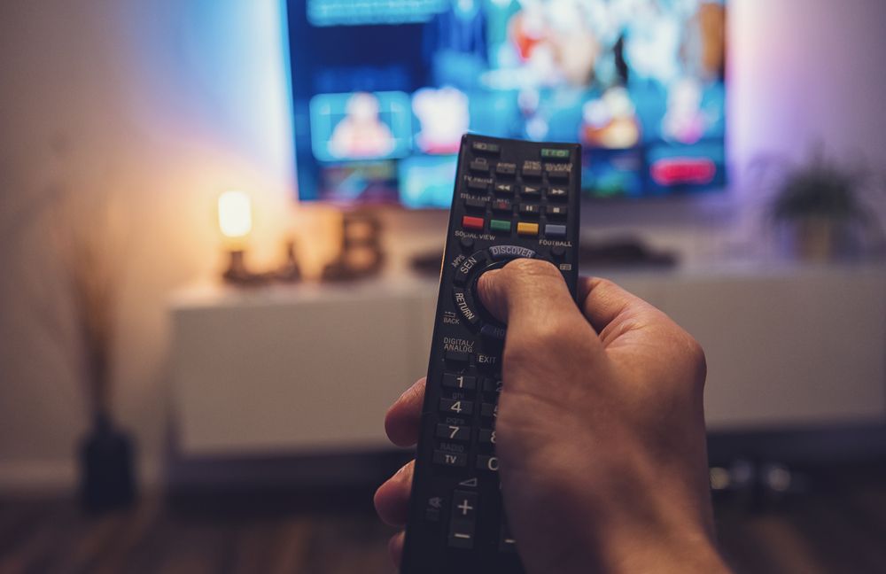 Hand Holding a TV Remote Toward a Blurred Television — MATV Systems Australia Pty Ltd in Wickham, NSW
