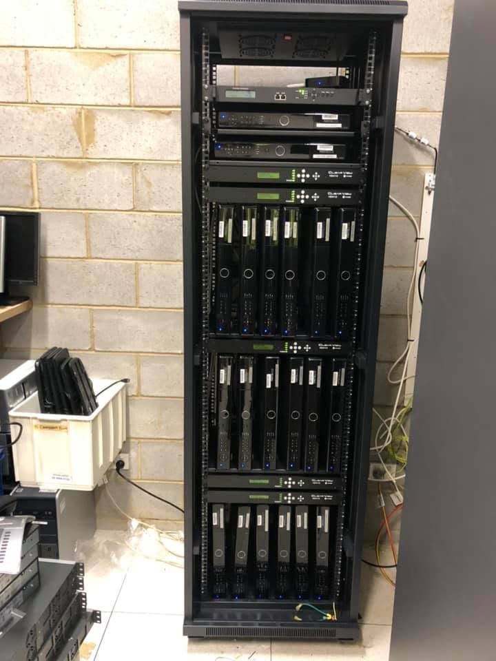 Tall black server rack with stacked network equipment against a cinderblock wall in a utility room — MATV Systems Australia Pty Ltd in Wickham, NSW