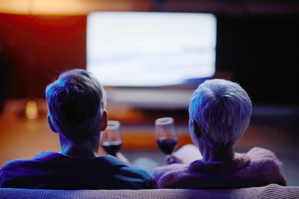 Two People Sit On A Couch Watching A Bright TV In A Dim Living Room — MATV Systems Australia Pty Ltd in Wickham, NSW
