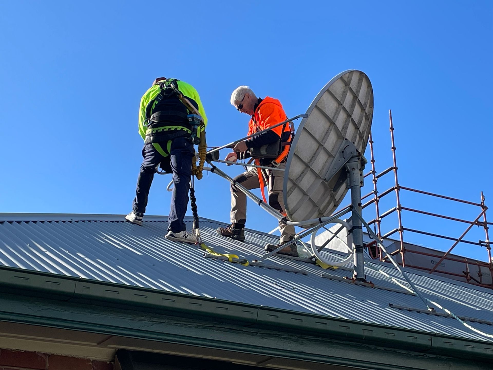 Two Workers on a Rooftop Installing a Satellite Dish, Wearing Safety Harnesses — MATV Systems Australia Pty Ltd in Wickham, NSW
