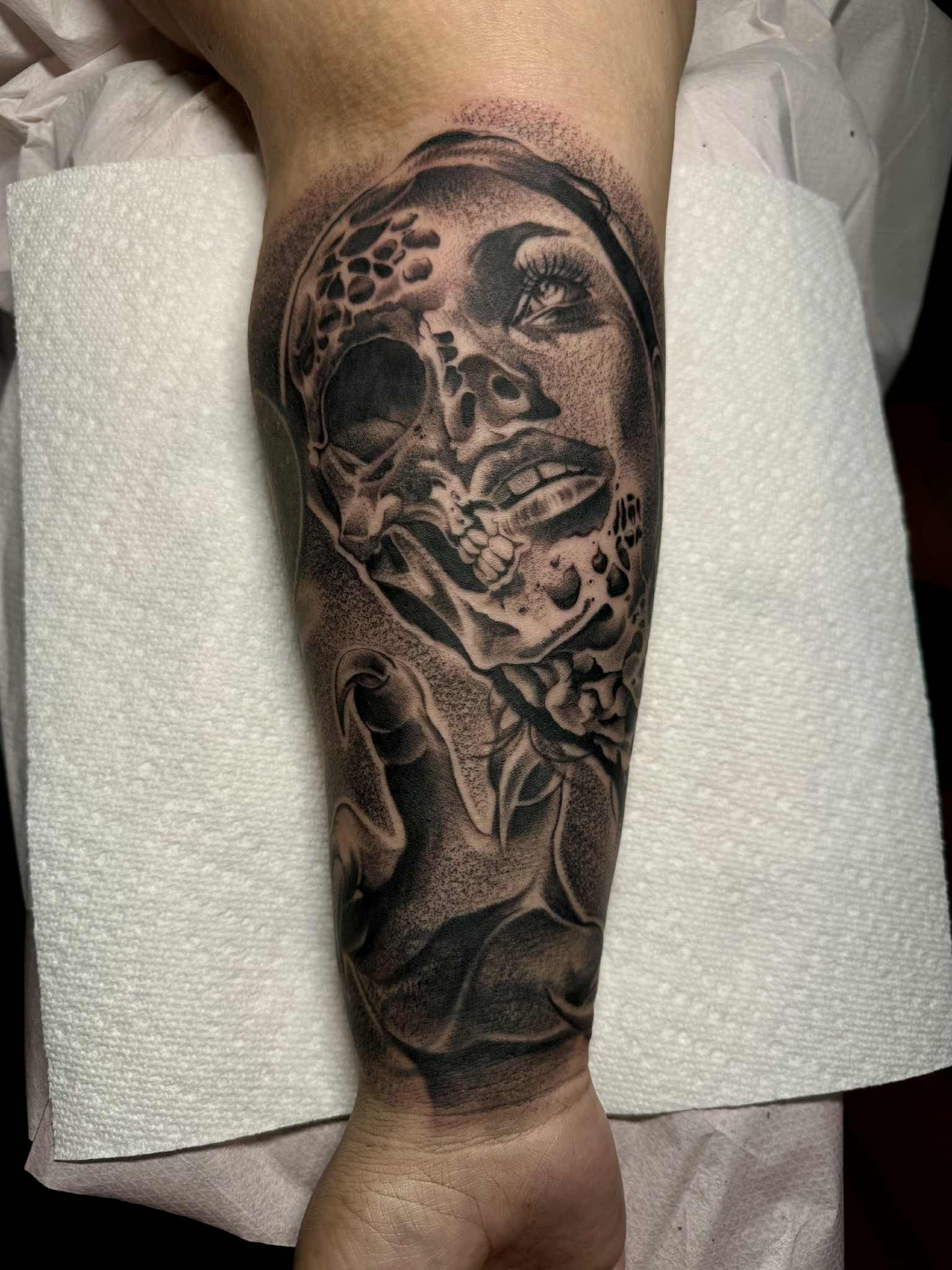 Tattoo of a face merging with a skull, with an outstretched hand, detailed grayscale art on forearm.