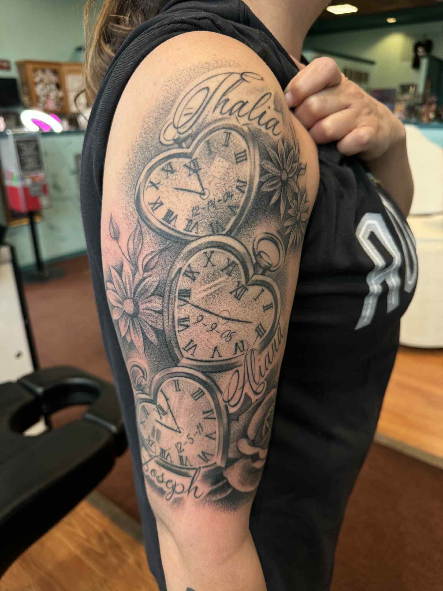 Woman's arm tattoo featuring heart-shaped clocks, flowers, and the name