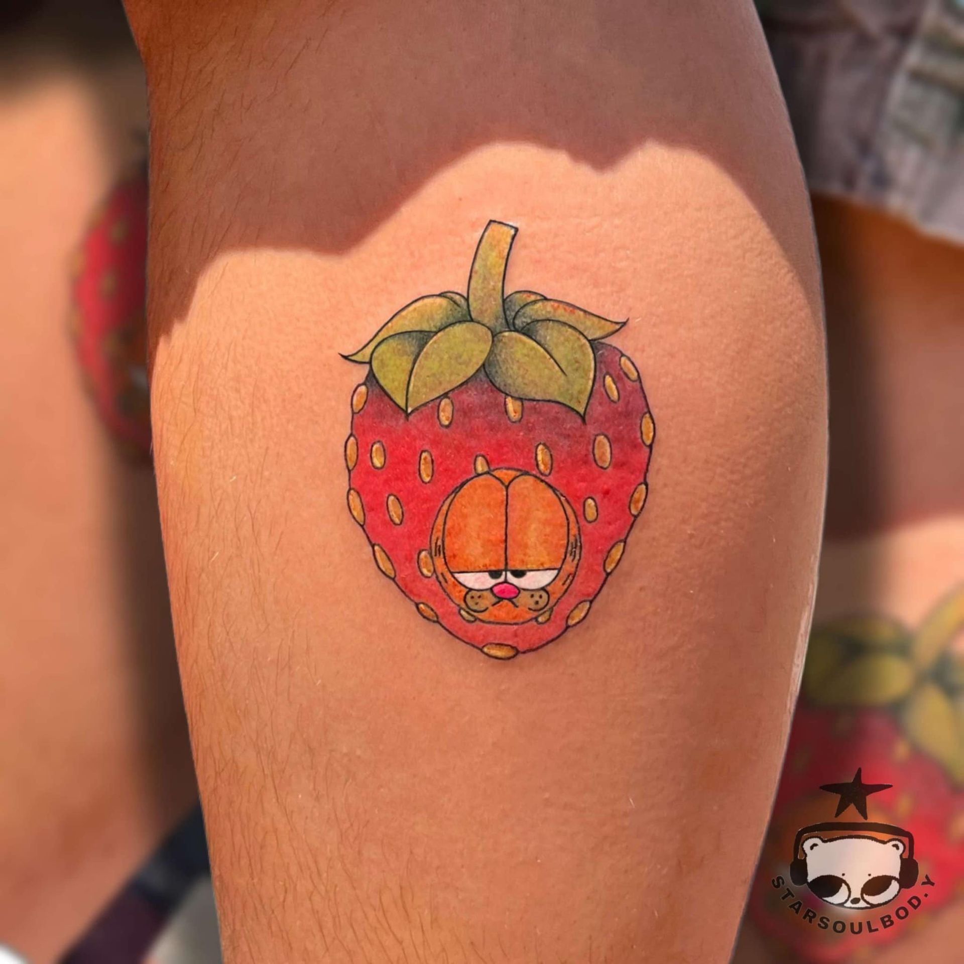 Tattoo of Garfield the cat's face inside a strawberry, on a person's leg.