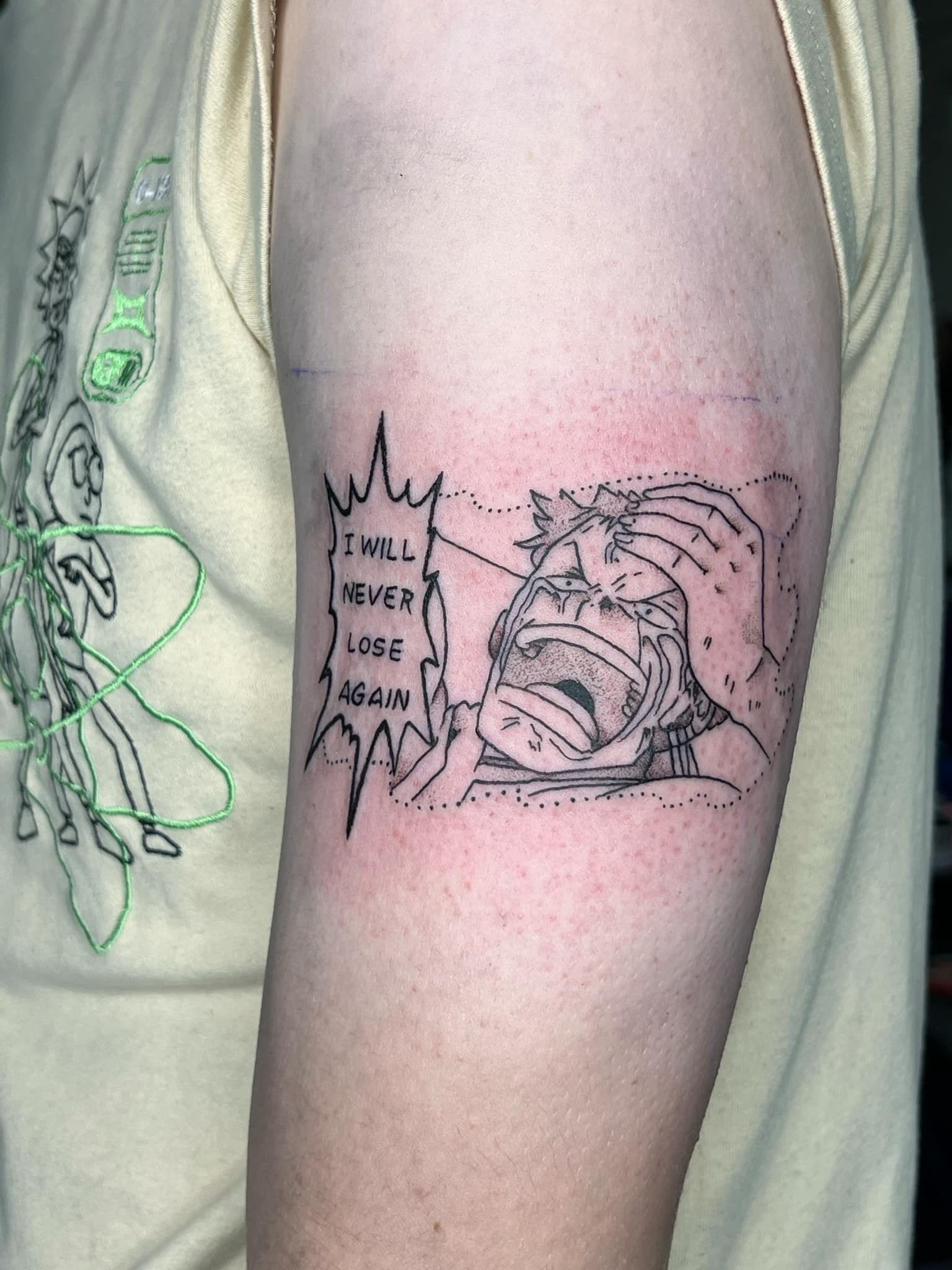 Tattoo on an arm with text “I shall never lose again!” and a cartoon character with a determined expression.