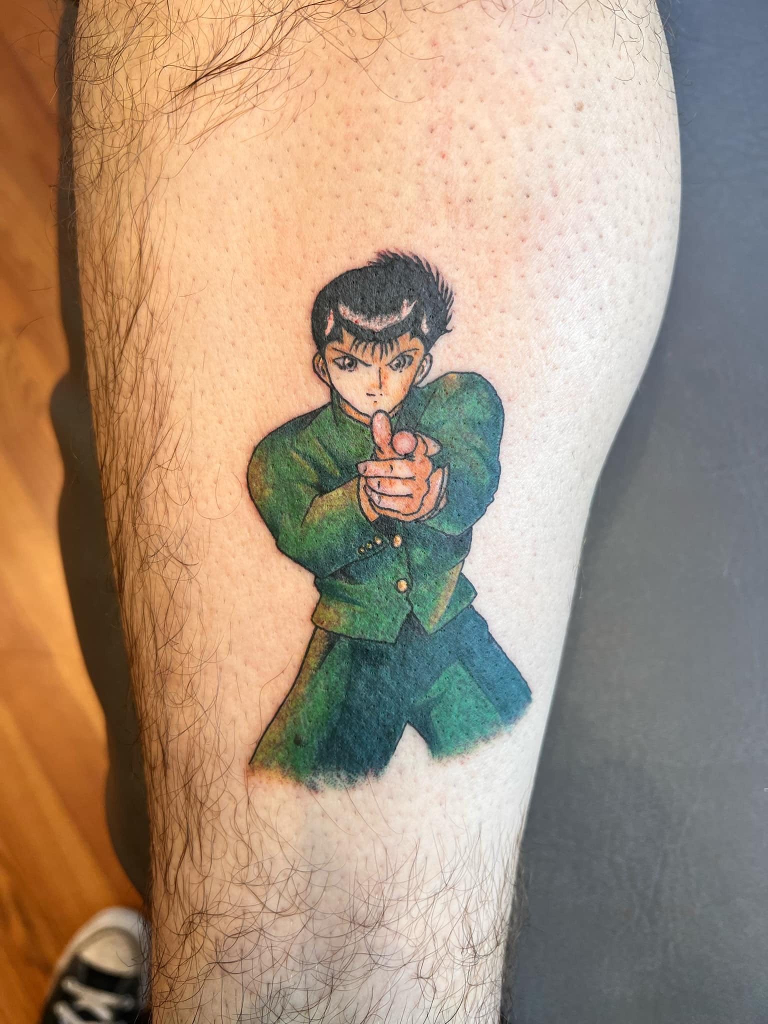 Tattoo of Yusuke Urameshi from Yu Yu Hakusho pointing his finger gun on a leg. Green jacket, dark hair.