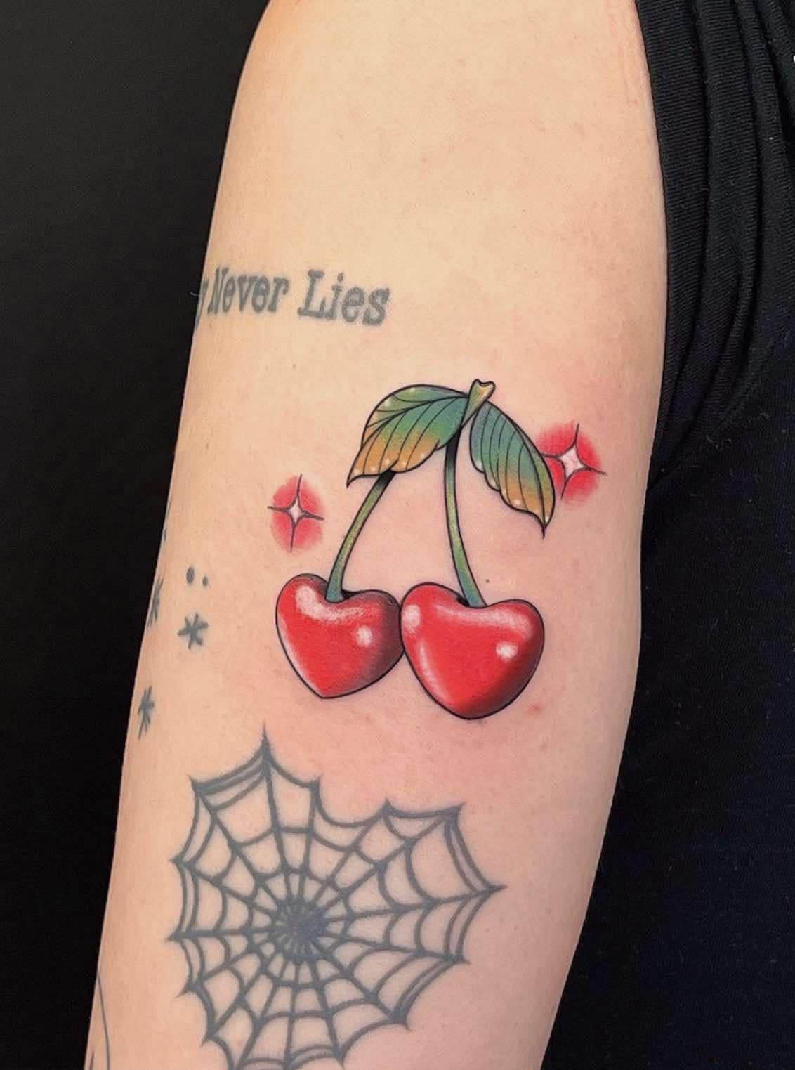 Tattoo of two red cherries with green leaves on a person's arm, surrounded by starbursts.