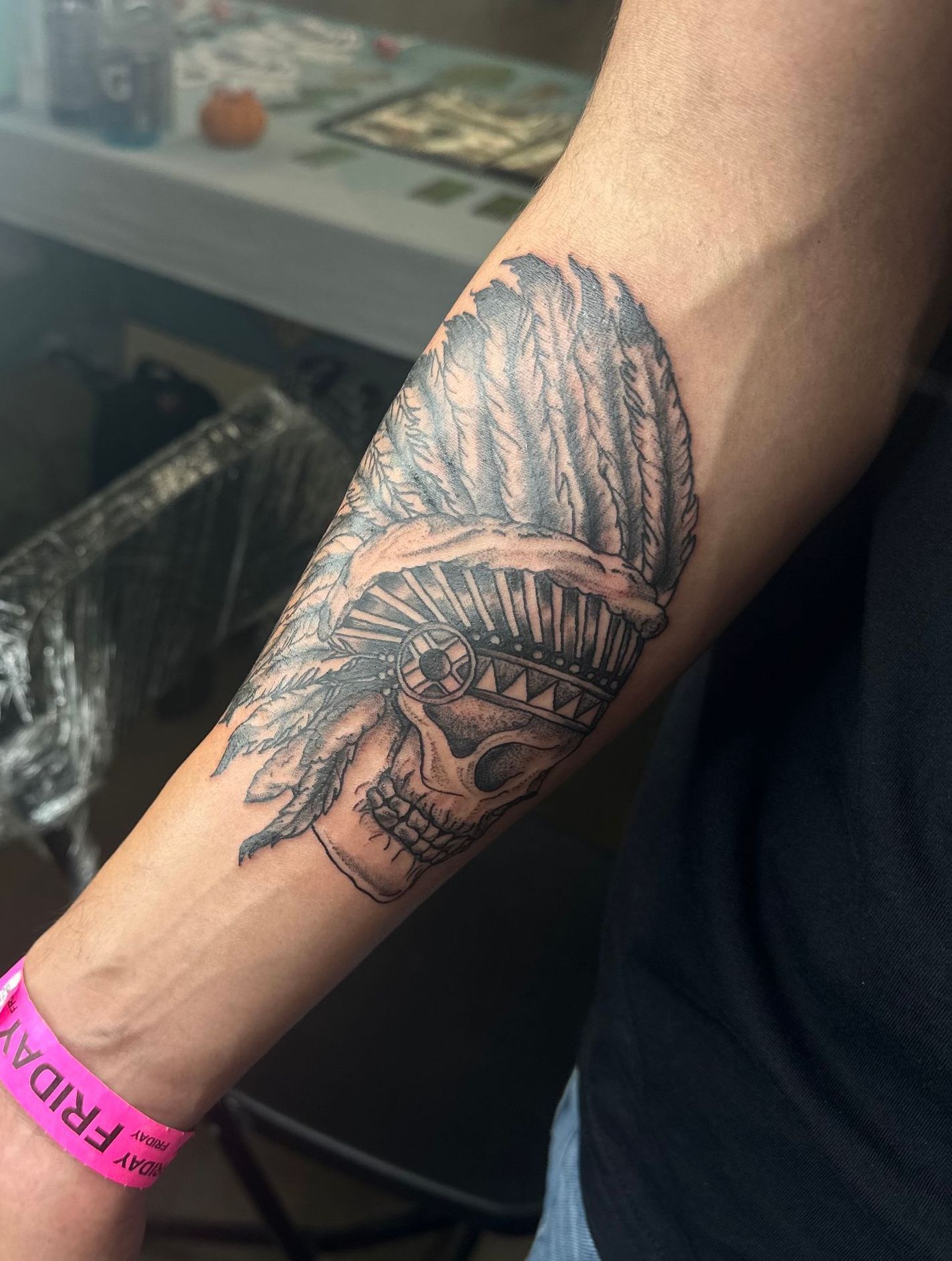 Tattoo on arm depicting a skull wearing a feathered headdress.