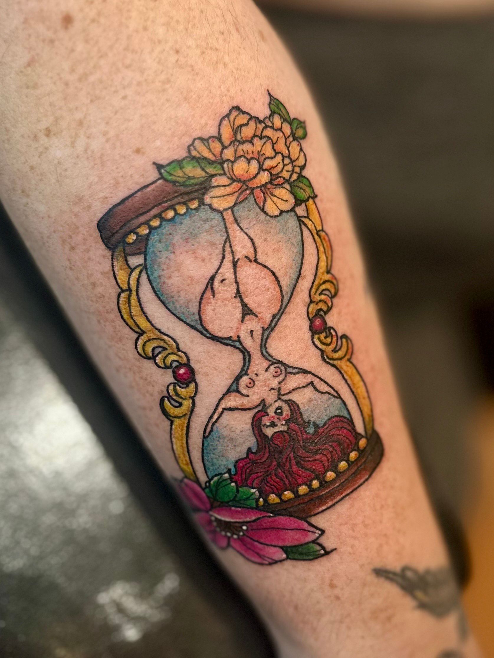 Hourglass tattoo with flowers, in the top half a torso and in the bottom a red figure.