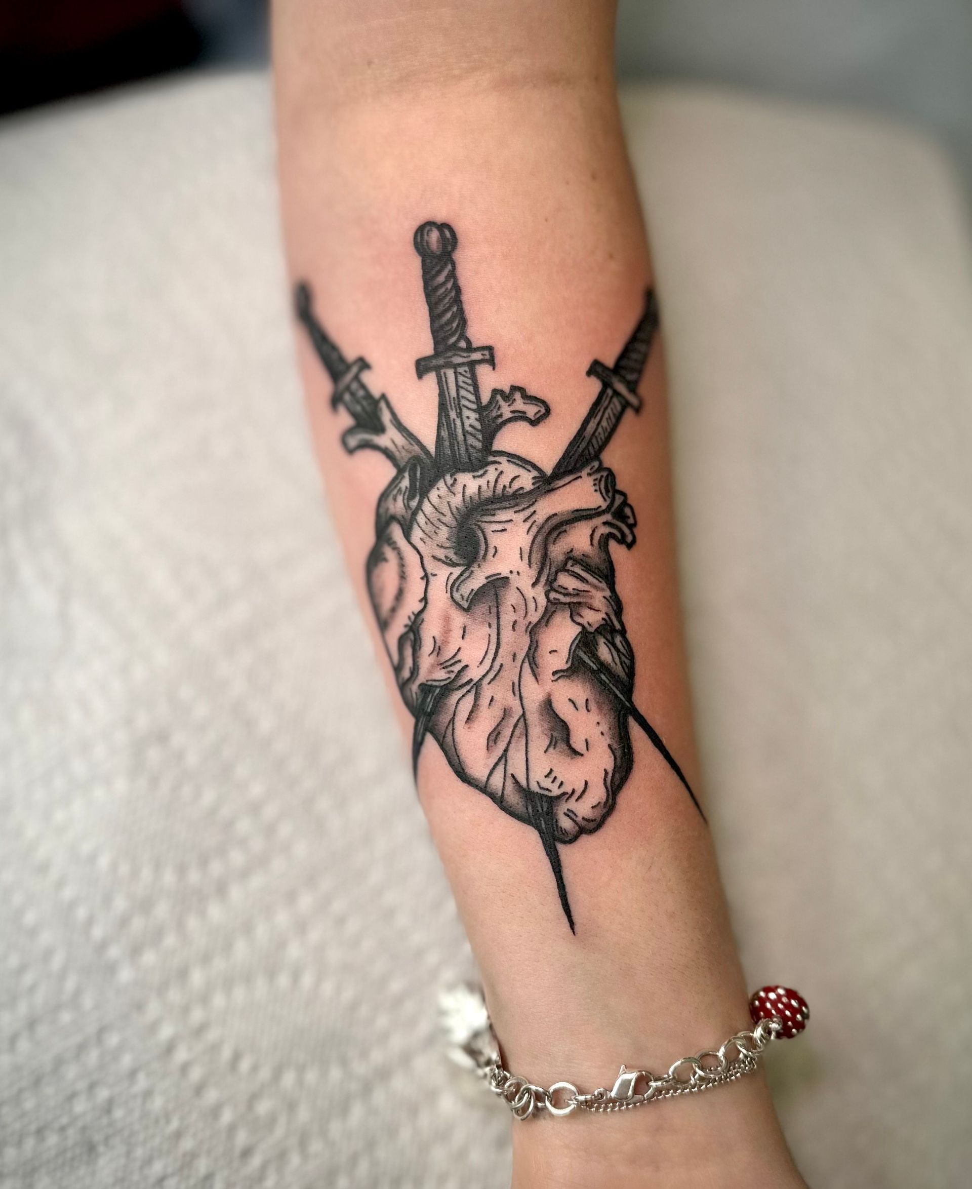 Tattoo of a human heart pierced by three swords on a forearm.