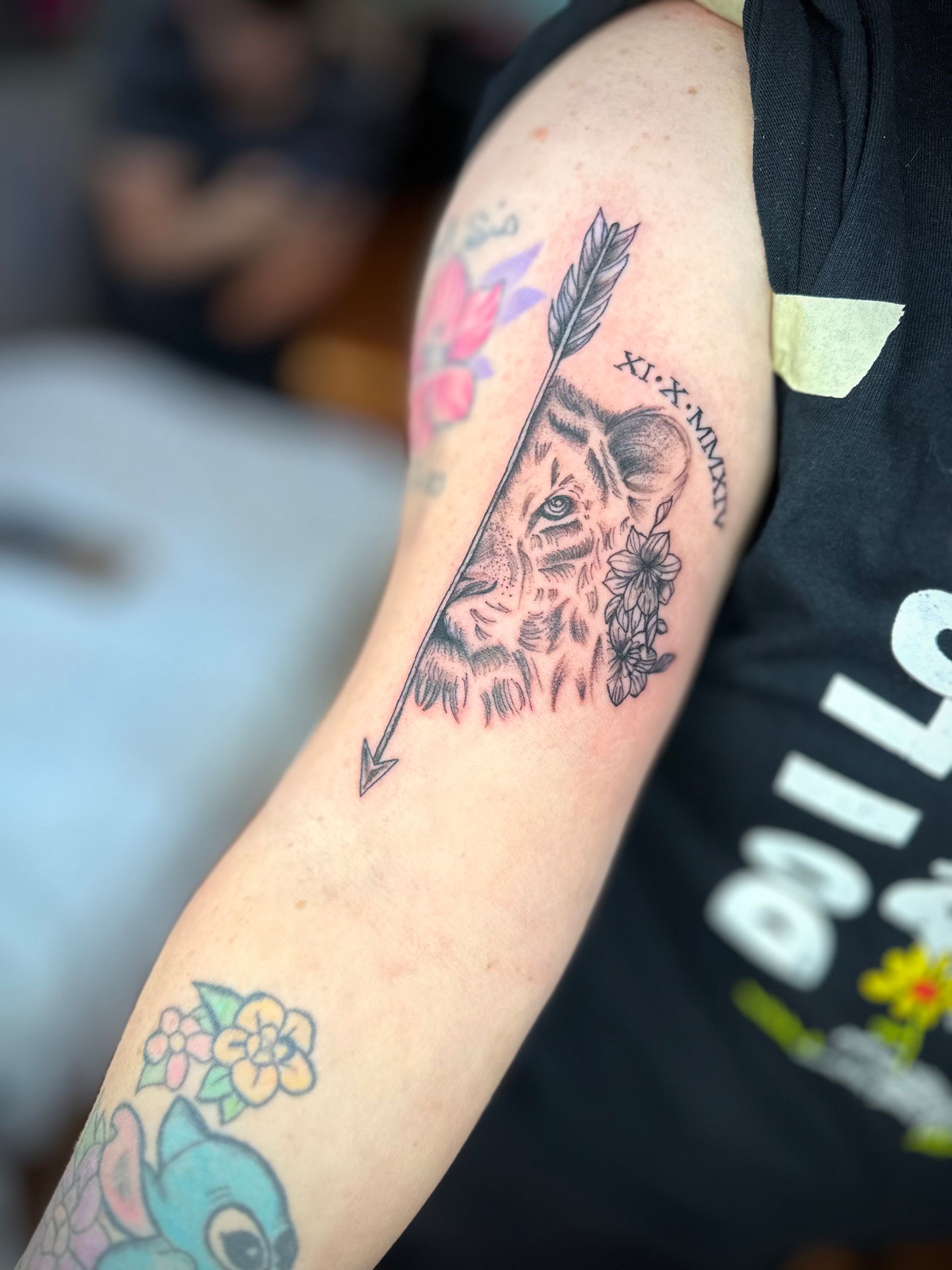 Tattoo of a lion's face pierced by an arrow, with Roman numerals, on a person's arm.
