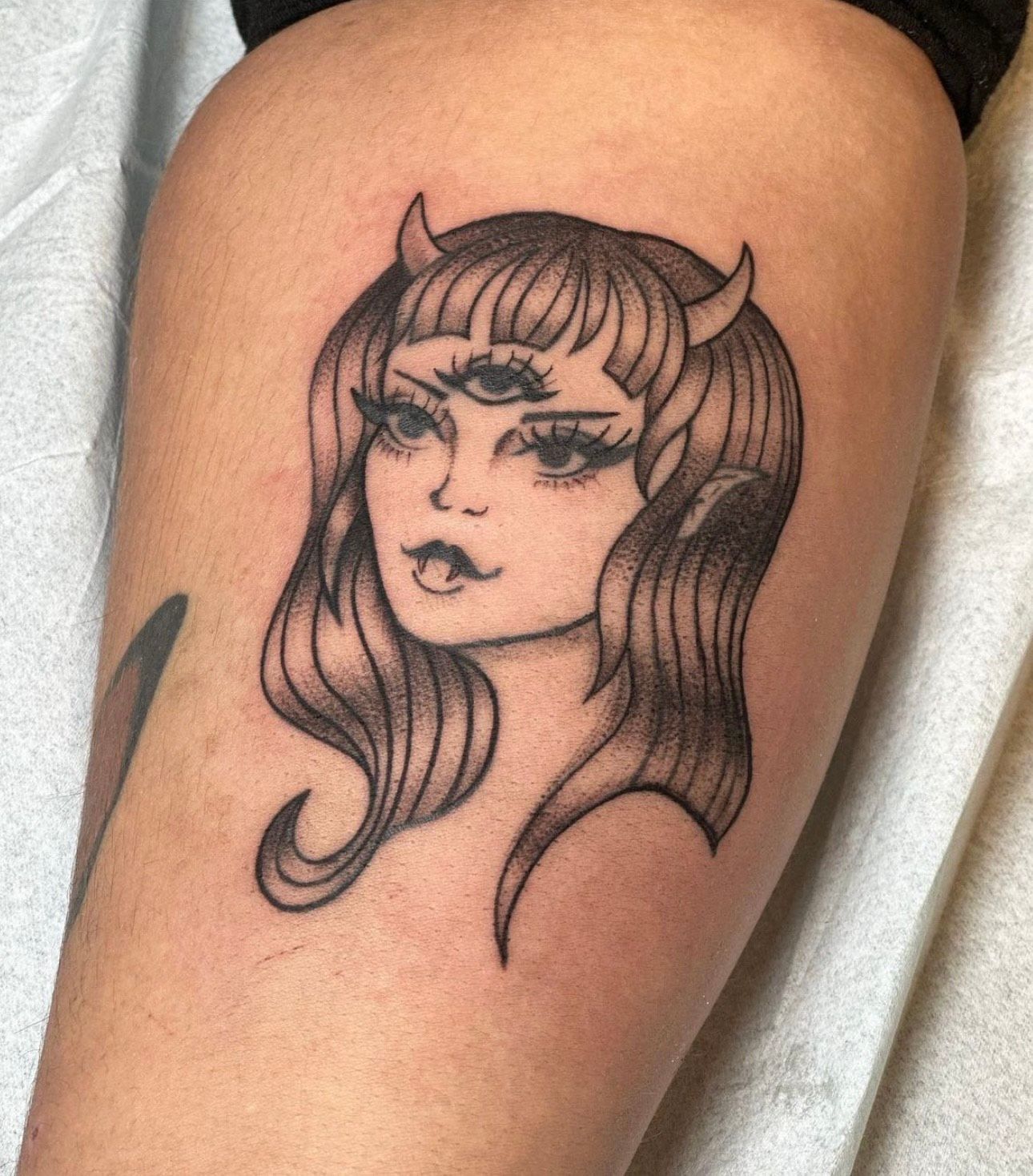 Tattoo of a woman with three eyes, horns, and flowing hair on a person's arm.