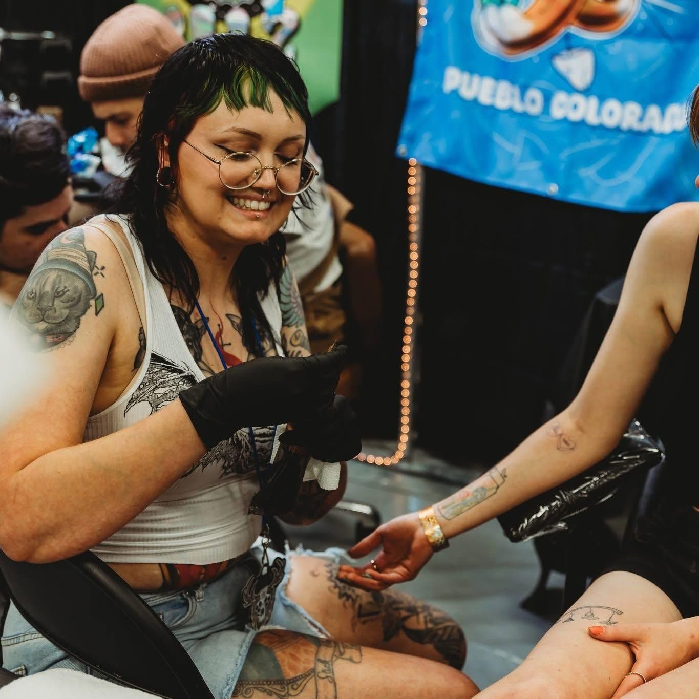 Tattoo artist giving a tattoo at a convention, with two assistants and a partially visible client.