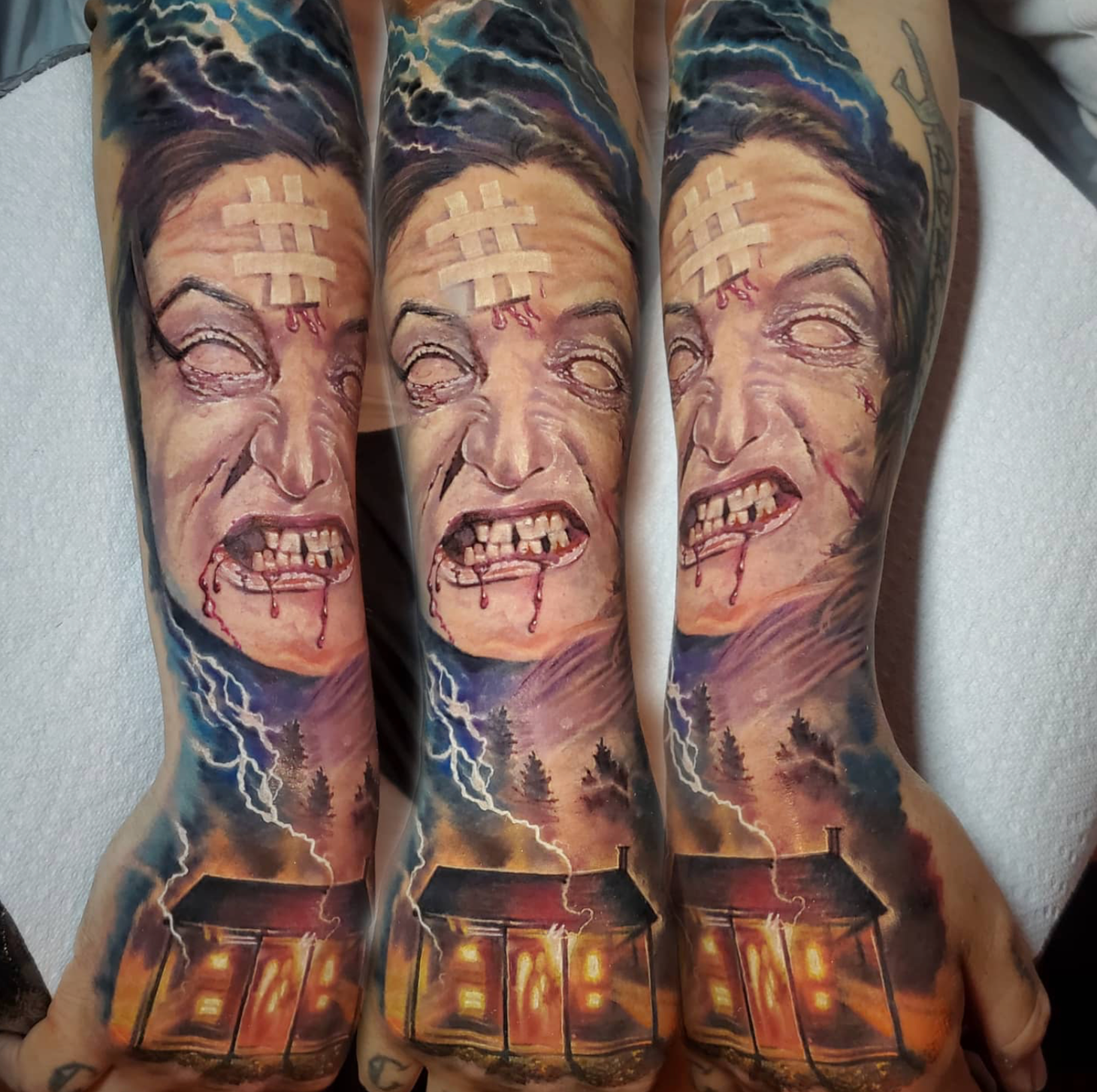 Tattoo of a monster face with a bloody mouth, a house with lit windows, and lightning in a dark sky.