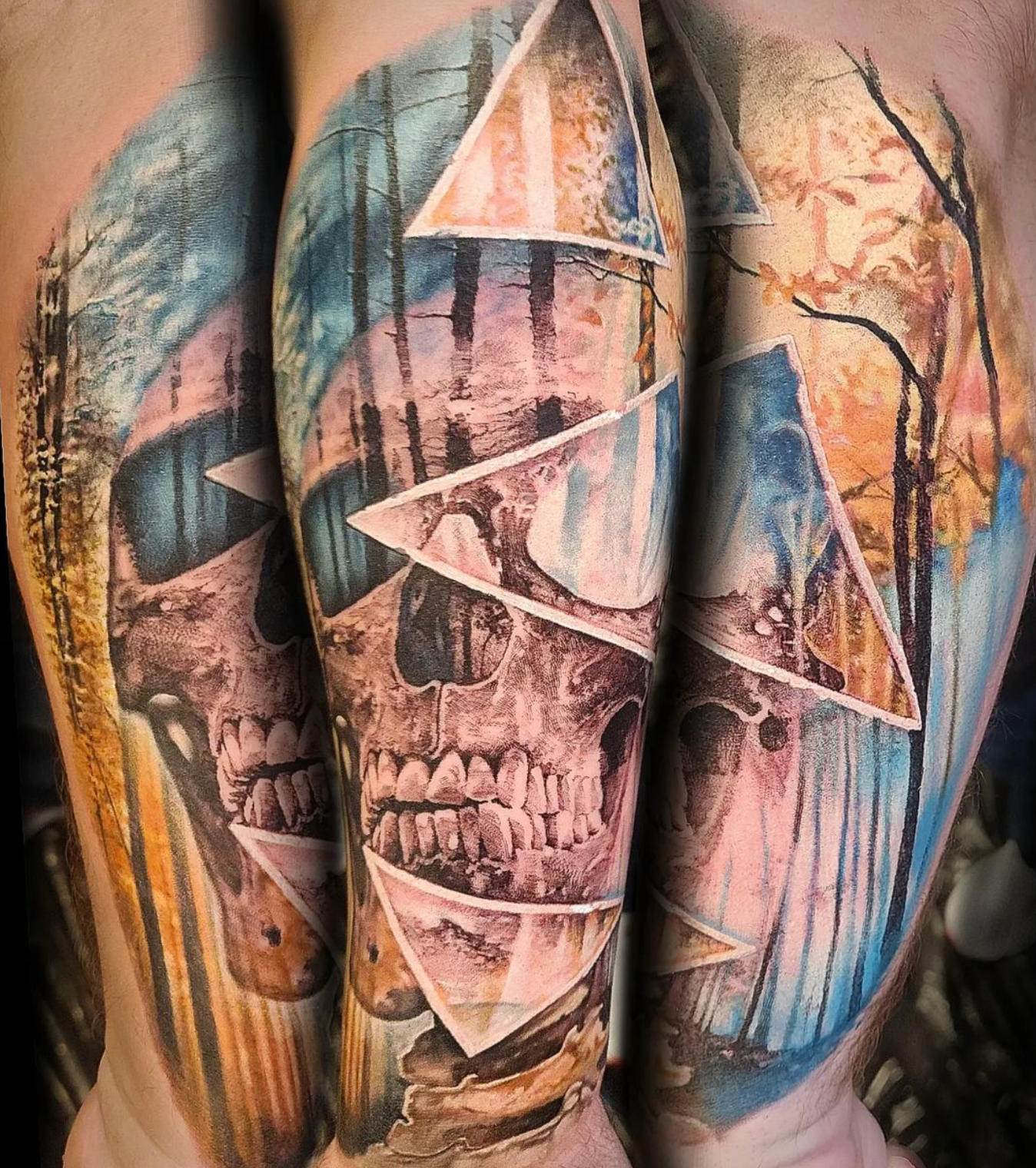 Colorful tattoo of a skull and forest scene with geometric triangles overlaying the design.