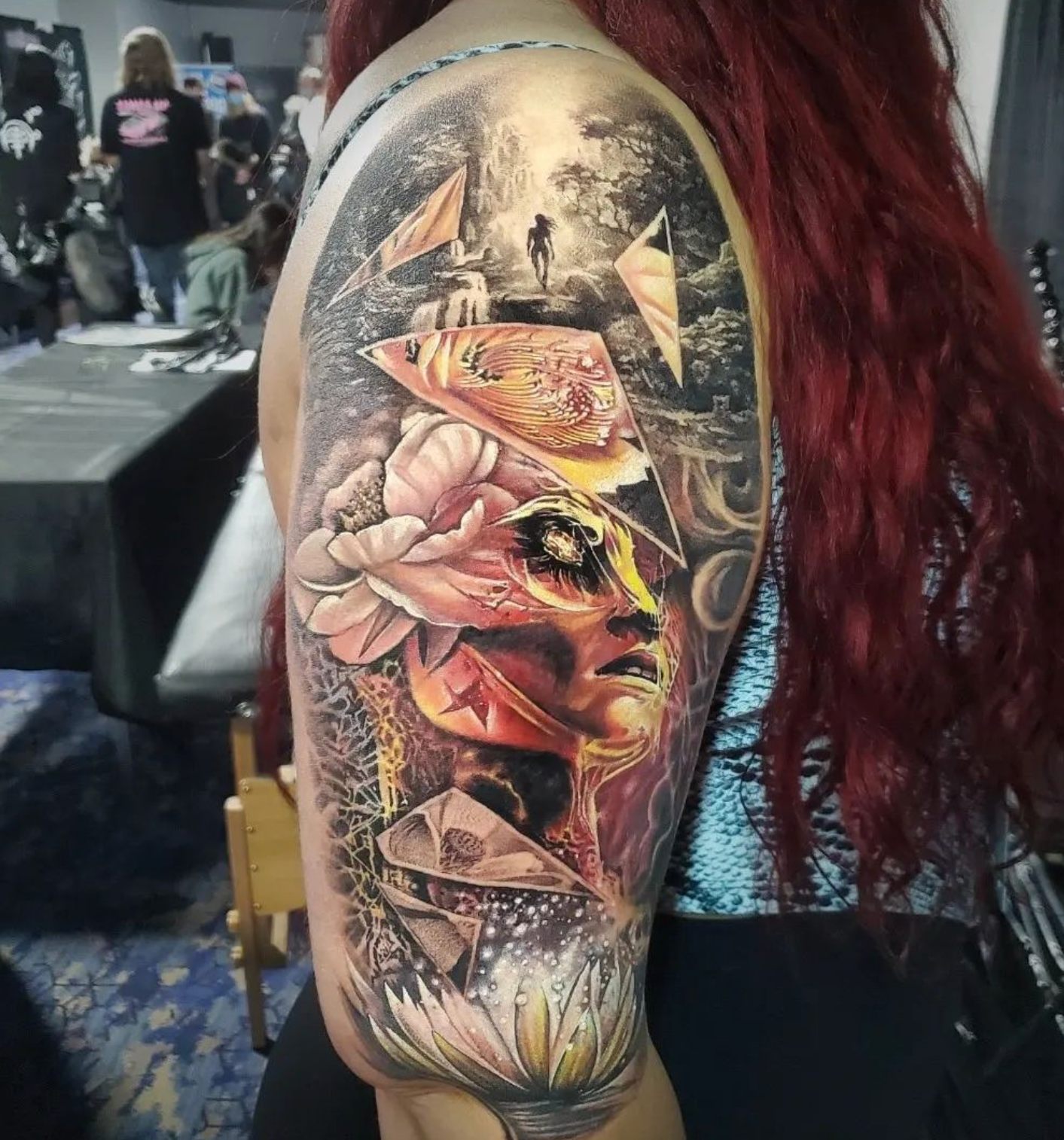 Woman's arm tattoo: portrait with flower, geometric shapes, and a forest scene, vibrant colors.