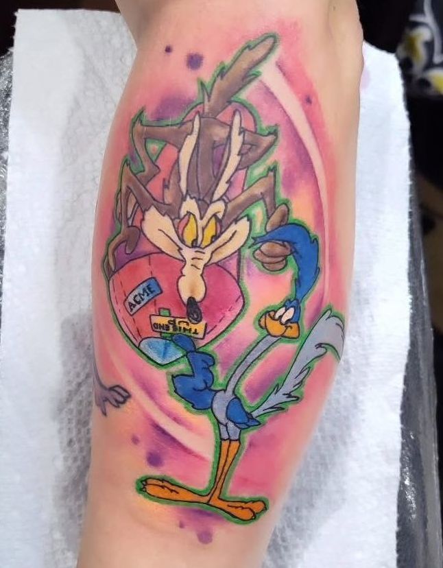 Tattoo of Wile E. Coyote and Road Runner, in front of a pink and purple background, on a person's arm.