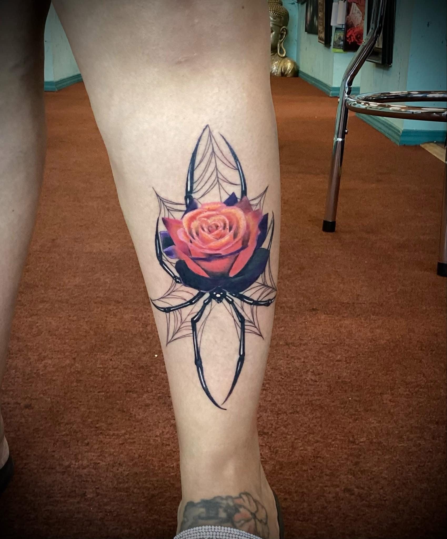 Tattoo of a vibrant rose on a calf, surrounded by black abstract lines. Brown carpet in the background.