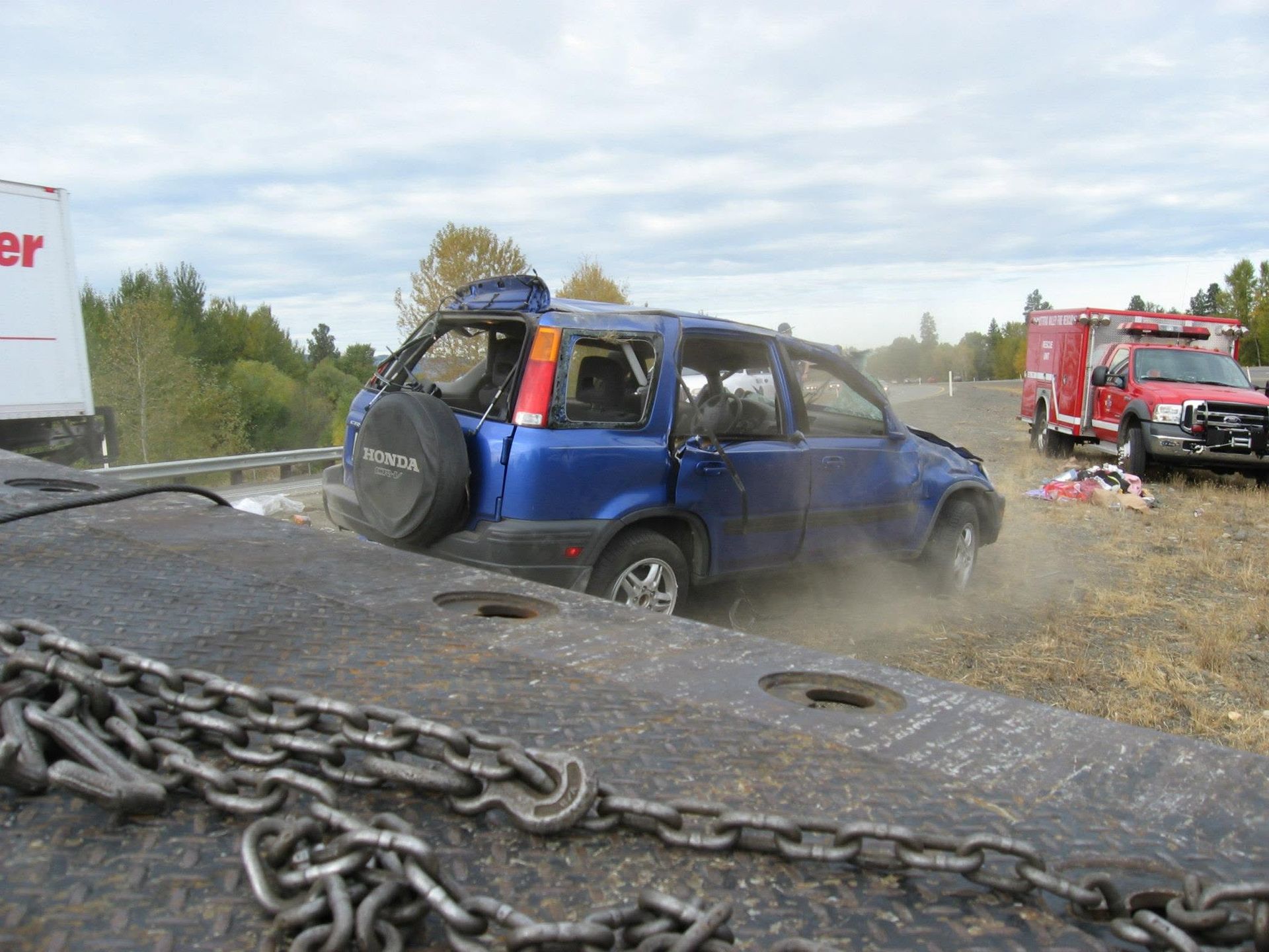 Blue SUV wrecked in roadside ditch, with a tow truck nearby and chains in the foreground