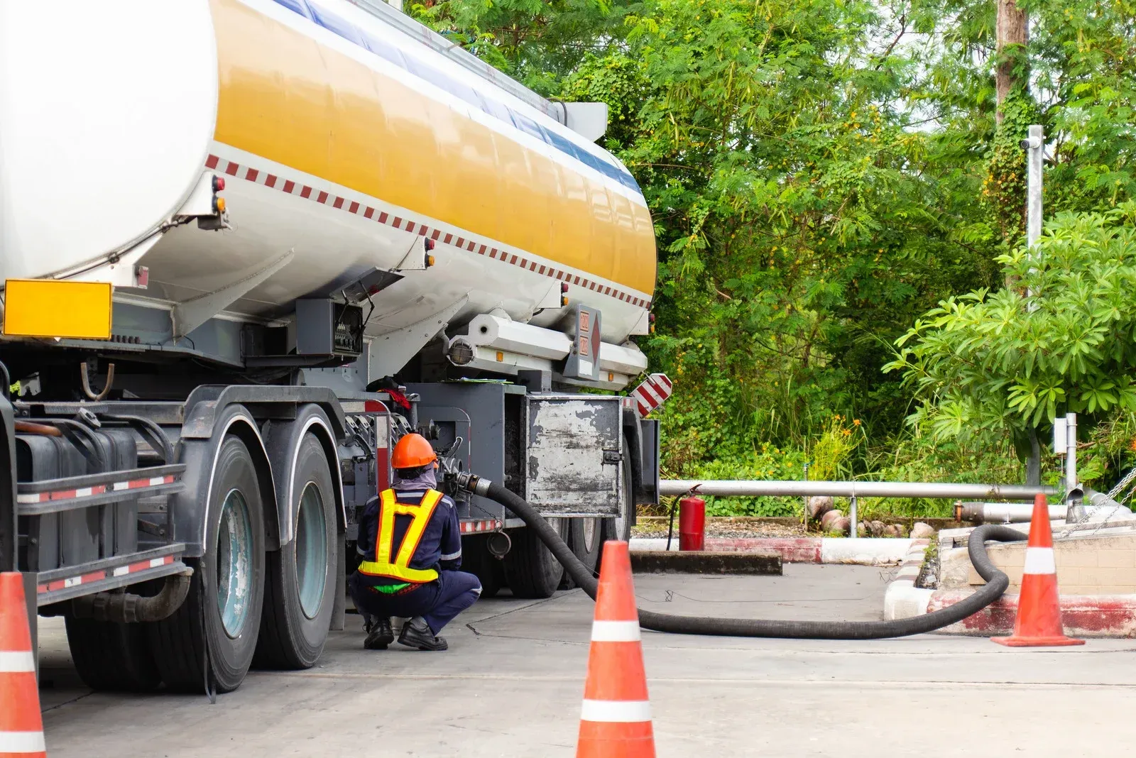 A man is kneeling next to a tanker truck in a parking lot.