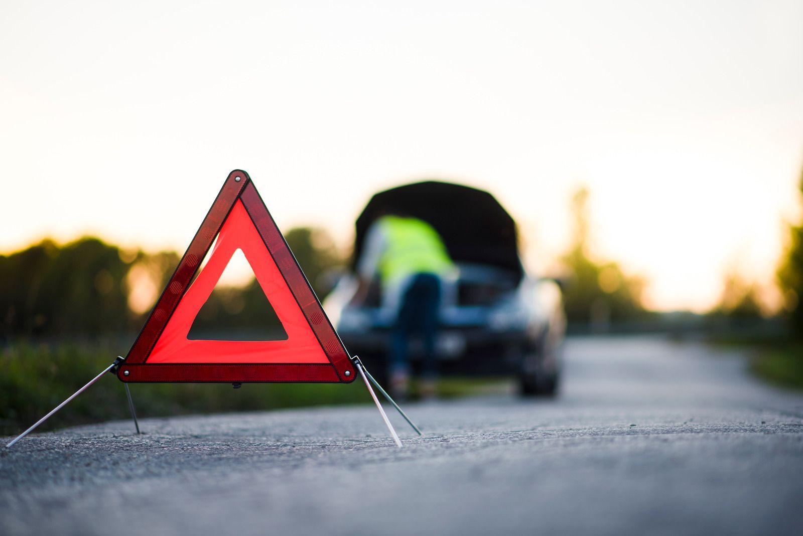 Red warning triangle on roadside with a blurred car in the background at sunset