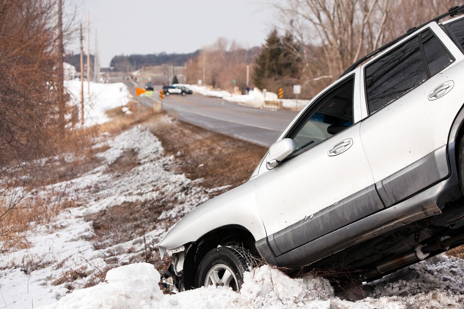 White SUV stuck in a snowy roadside ditch beside a rural road