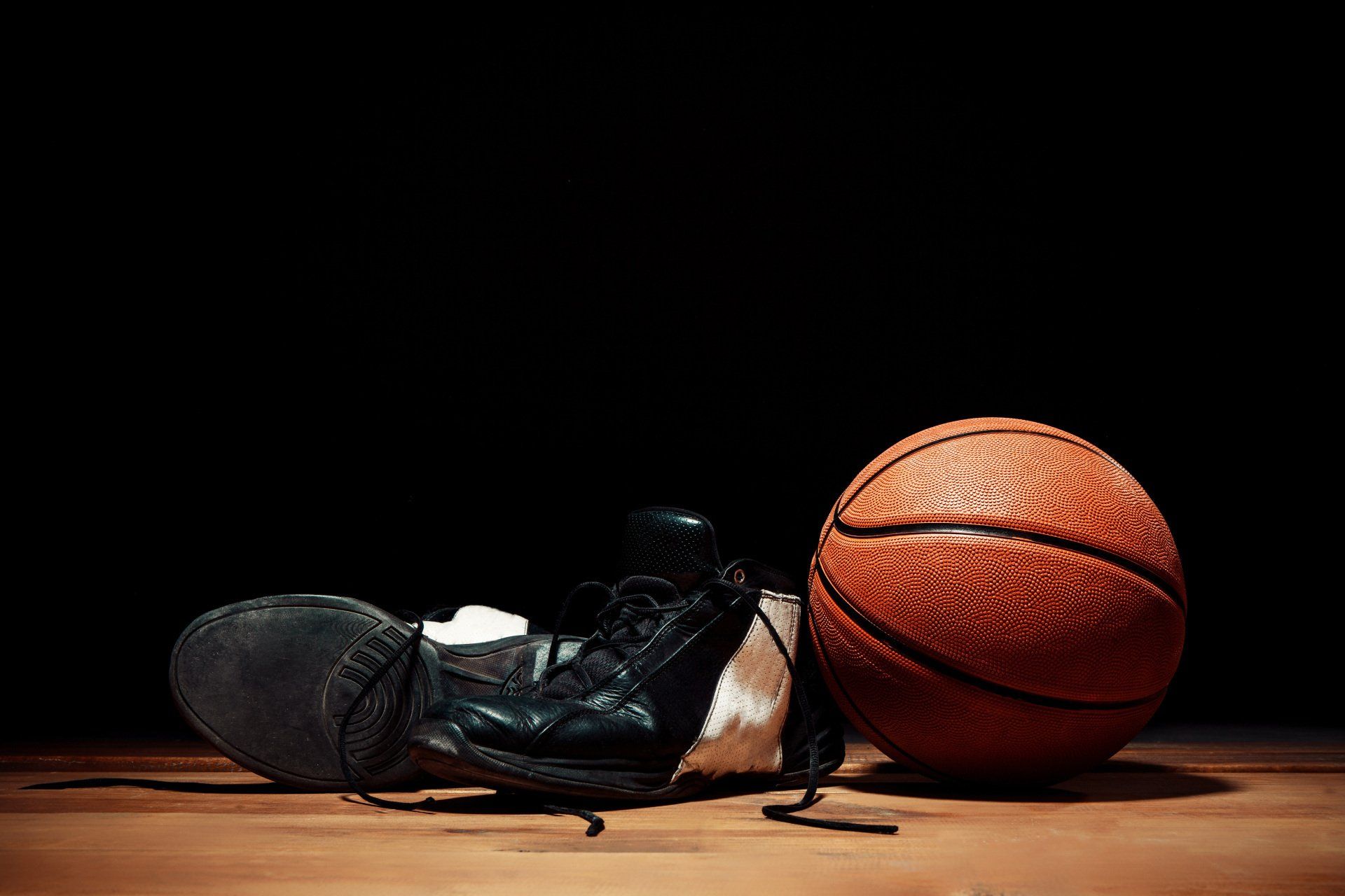 A basketball and a pair of shoes are on a wooden floor.