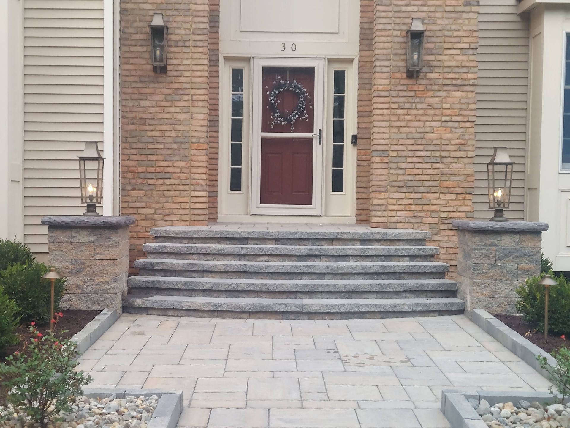 Stone stairs leading up from a paved patio to a grassy lawn, framed by a matching segmental retaining wall.