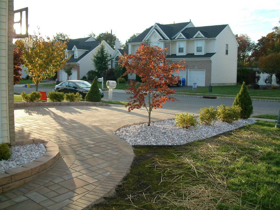 A paved walkway curves toward a front entrance, flanked by a landscaped garden bed with white stone, shrubs, and a tree. A paved walkway curves toward a front entrance, flanked by a landscaped garden bed with white stone, shrubs, and a tree.