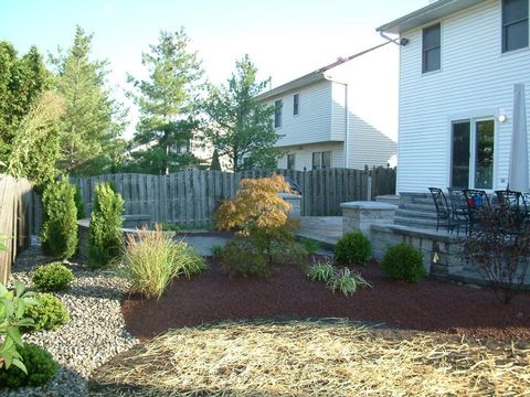 A backyard with a stone patio, red mulch garden beds, small evergreen shrubs, a Japanese maple, and a white house. A backyard with a stone patio, red mulch garden beds, small evergreen shrubs, a Japanese maple, and a white house.